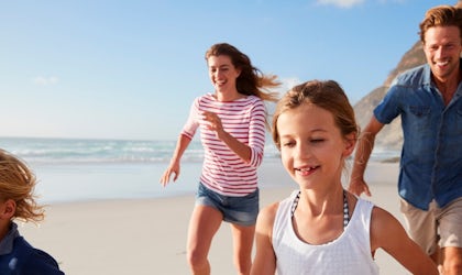 ung familie med mor, far og to barn som løper i sommerklær på strand