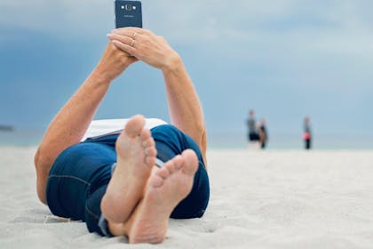 kvinne som ligger på Sandvesanden på Karmøy og surfer på mobilen