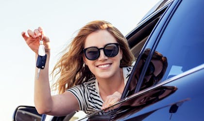 smilende kvinne som ser ut av bil og holder bilnøker.