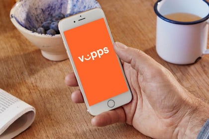 bord med kaffekopp, avis og bær og hånd som holder mobil der vipps er på skjermen