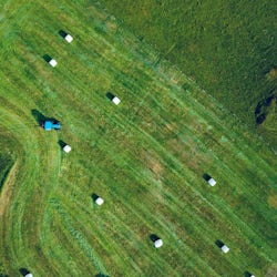 traktor sett ovenfra på grønne marker torvastad med høyballer spredt rundt.