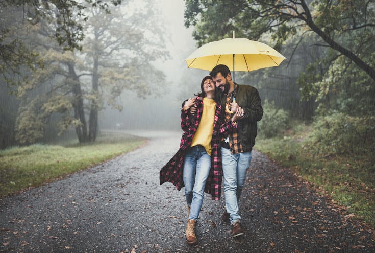 Et par som går under en gul paraply i regnvær