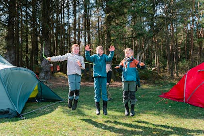 Tre barn som hopper mellom to telt