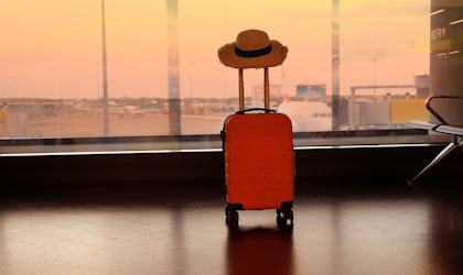 Bilde av koffert og solhatt som står i en avgangshall.
