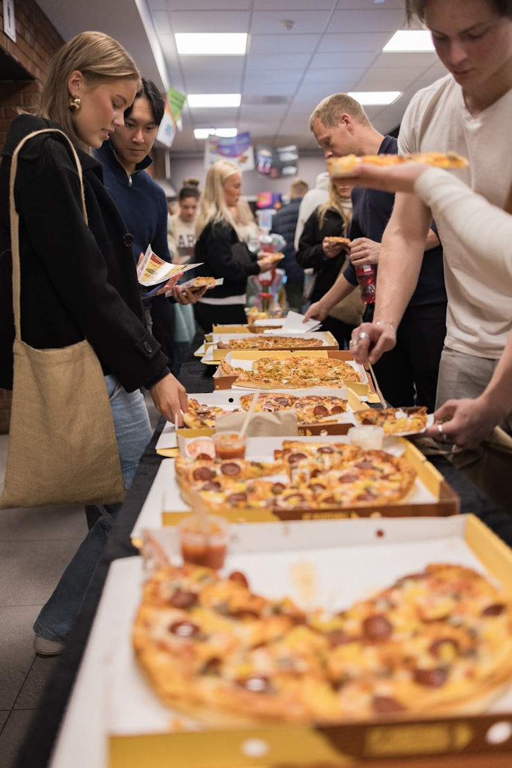 Langt bord med mange deltakere som forsyner seg med pizza