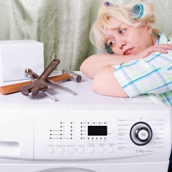 Kvinne med hårruller og verktøy er oppgitt over ødelagt vaskemaskin.