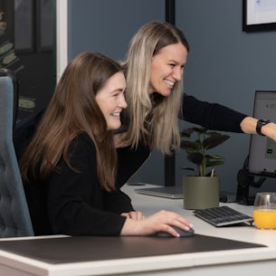 To kollegaer sitter foran dataskjermen, og hun enen peker mot skjermen.